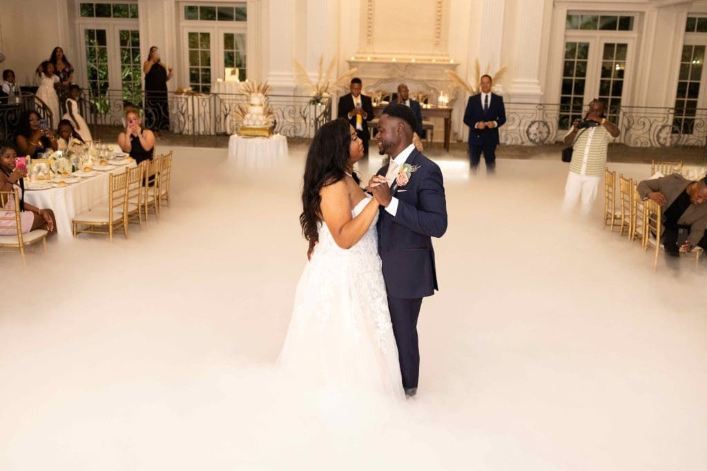 Bride and groom dancing on a cloud-like fog at their wedding reception surrounded by guests.